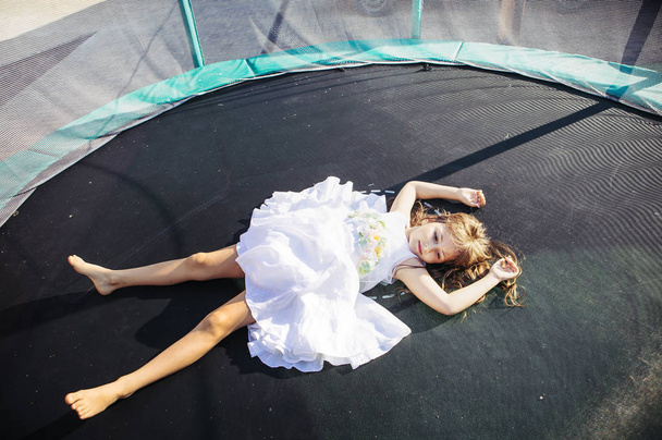 Cute girl in white dress having fun on trampoline - Foto, imagen