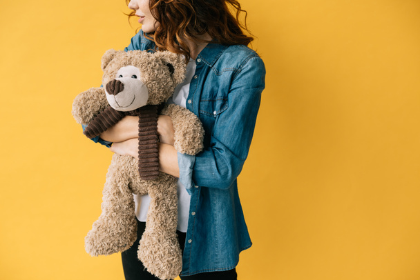 cropped view of redhead girl hugging teddy bear and standing on orange  - Photo, Image