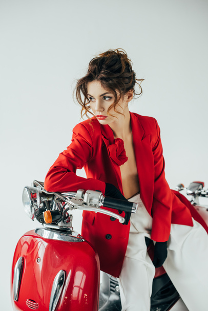 serious and stylish young woman sitting on red motorcycle on white - Zdjęcie, obraz