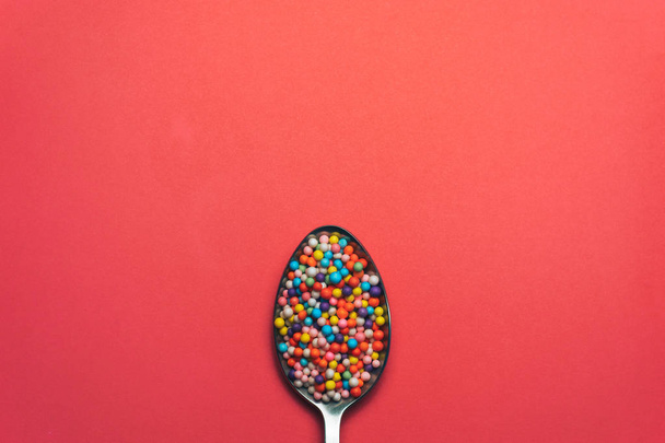 lepel gekleurde preparaten (vitaminen, kleurstoffen, smaakversterkers, voedingssupplementen, innovatieve technologie, Candy Sweets) op een rode achtergrond. - Foto, afbeelding
