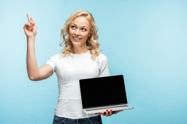 mujer rubia feliz sosteniendo el ordenador portátil con la pantalla en blanco y el gesto en azul
  - Foto, Imagen