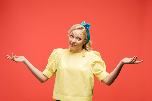 confused blonde woman in blue headband standing and gesturing on red  - Фото, зображення