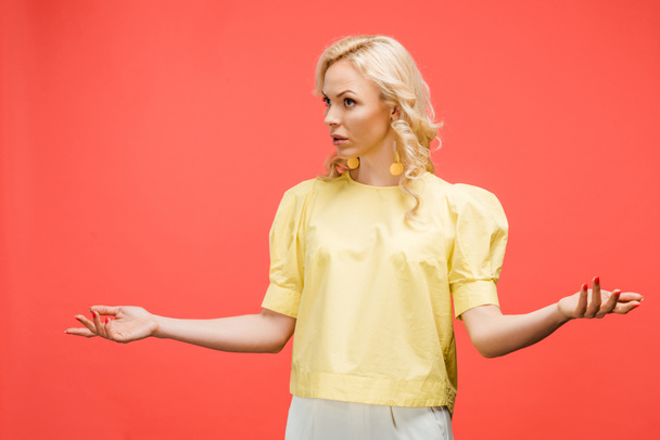 Verwirrte blonde Frau steht mit ausgestreckten Händen auf rot  - Foto, Bild
