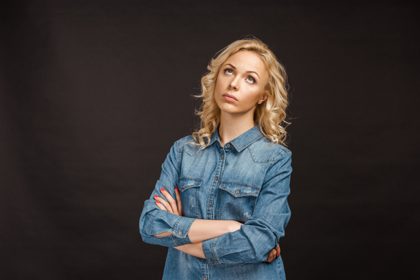 sad curly blonde woman standing with crossed arms on black - Zdjęcie, obraz