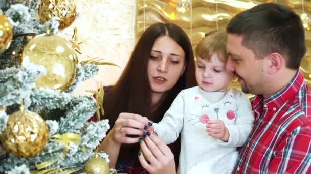 young parents with toddler daughter put ornament on Christmas tree at home - Video