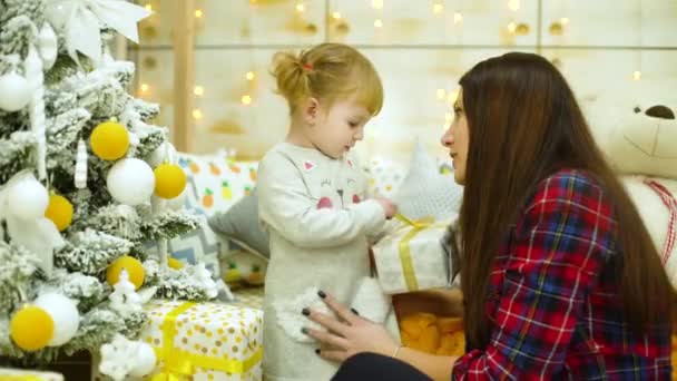 little girl with mother unpacking gift boxes near Christmas tree at home - Footage, Video