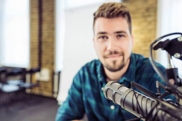 Atrakcyjny młody człowiek mówienie do mikrofonu. Człowiek i podcast Host rozmowa z mikrofonem. - Zdjęcie, obraz