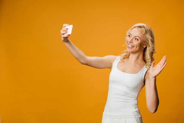 vidám szőke nő integetett kézzel, míg figyelembe selfie narancssárga  - Fotó, kép