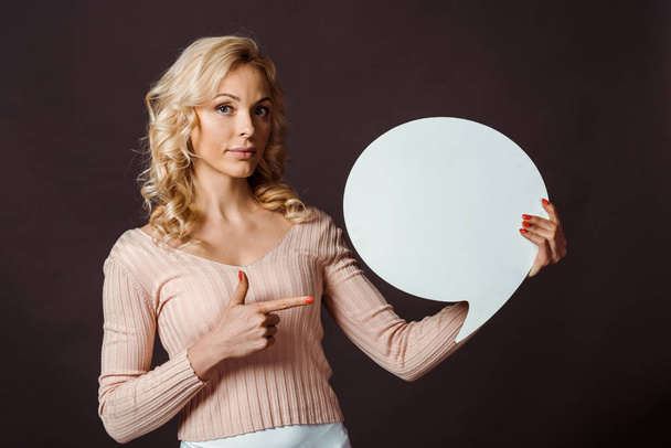 attractive blonde woman pointing with finger at speech bubble isolated on black  - Foto, imagen