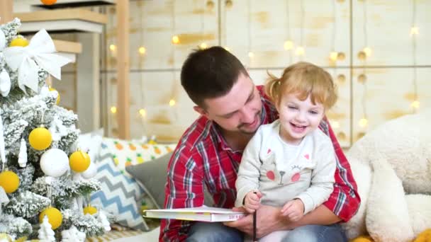 little girl sits on her father lap and has fun with pencils near Christmas tree - Záběry, video