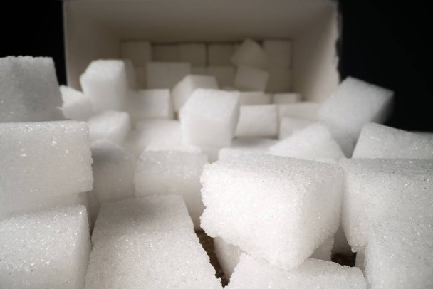 Tahta masa üzerinde karton kutu yanında şeker küpleri Makro atış. Sağlıksız gıda tatlandırıcı, tatlı kristal küpler - Fotoğraf, Görsel