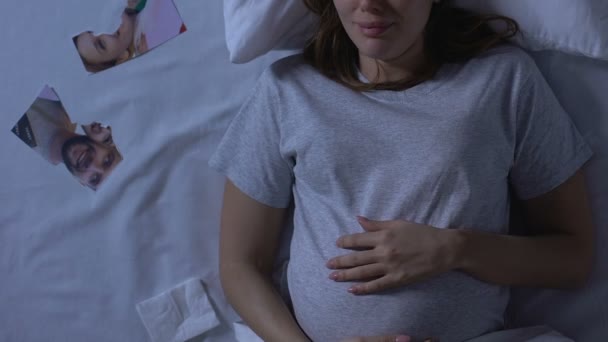 Pregnant woman crying in bed, torn family photo nearby, betrayal and divorce - Materiał filmowy, wideo