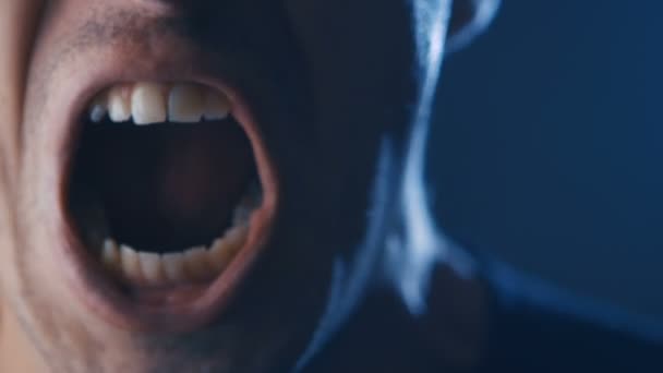 Agressieve man met boos gezichtsuitdrukking schreeuwen hardop in het donker. Close-up van man schreeuwen met mond wijd open. - Video