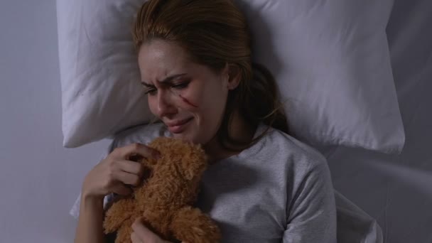 Lady with wounded face hugging teddy bear, crying in bed, victim needs support - Filmmaterial, Video