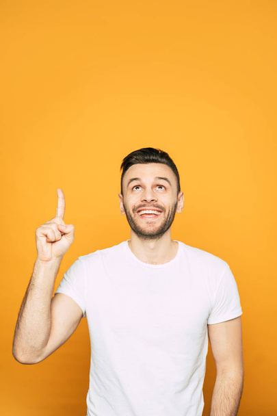 An orange background with a man next to it in basic T-shirt who is pointing on something what makes him feel pleasant - Foto, imagen