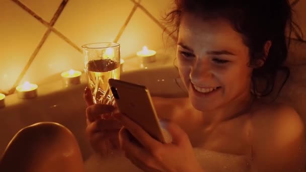 jong meisje neemt een bubbelbad met een smartphone, lacht gelukkig aanraken van het scherm - Video