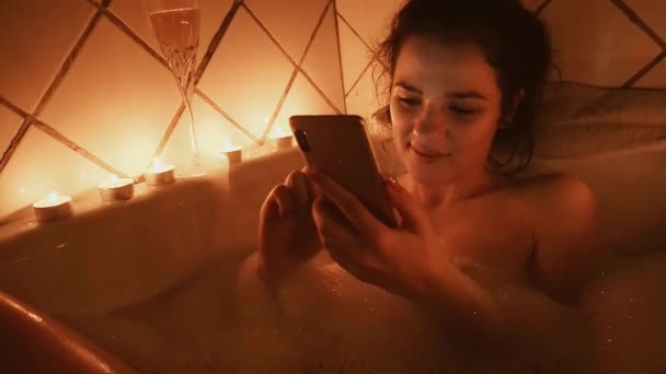 νεαρή κοπέλα παίρνει ένα αφρόλουτρο με ένα smartphone, γελάει ευτυχώς αγγίζοντας την οθόνη - Πλάνα, βίντεο