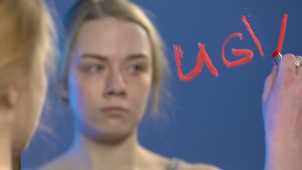 Upset teen girl writing with lipstick word ugly on mirror, low self-esteem - Felvétel, videó