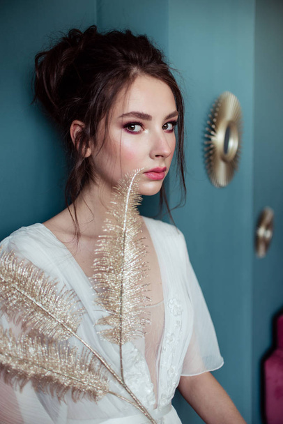 beautiful bride holding golden decorative feathers and leaning on green wall  - Фото, зображення