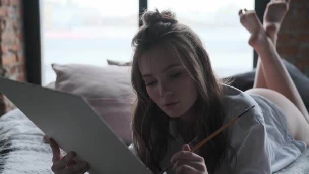 artist paints a picture lying in bed. portrait of an attractive girl painter - Filmagem, Vídeo