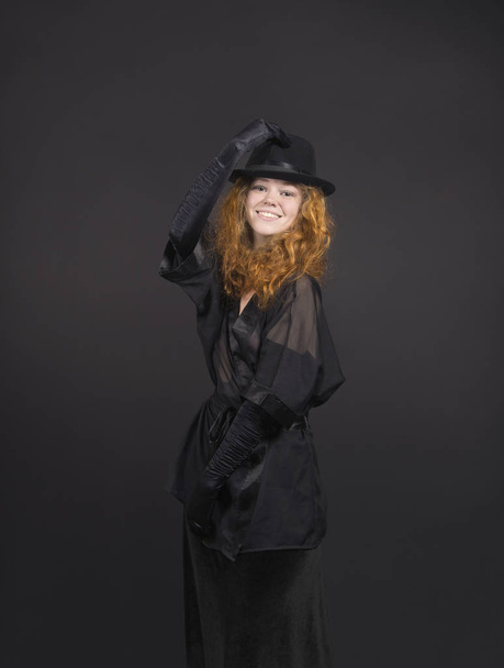 Emotional,red-haired girl in a black skirt,black blouse, black hat and black gloves. - Photo, image
