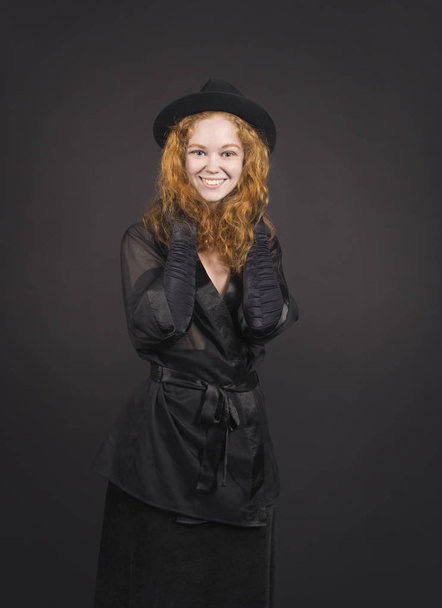 Emotional,red-haired girl in a black skirt,black blouse, black hat and black gloves. - Foto, immagini