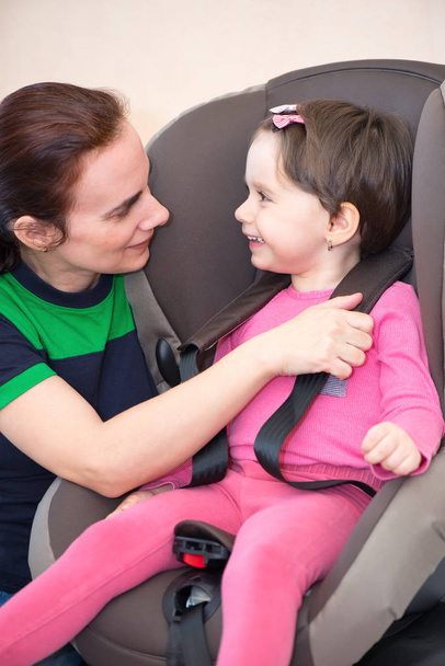 Moeder beveiligen dochter in de autostoel, geïsoleerd met uitknippad - Foto, afbeelding