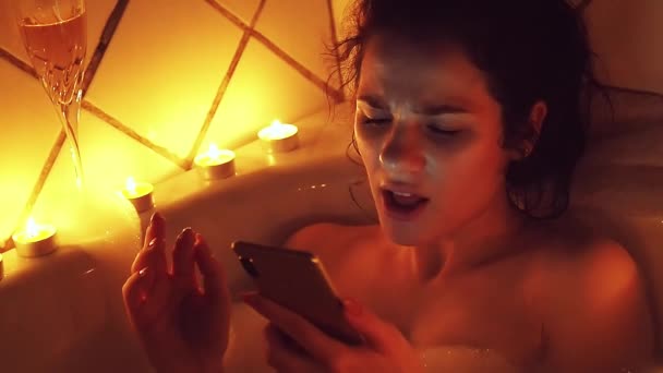 Молодая девушка поет, слушая музыку и глядя на экран смартфона в пенной ванне
 - Кадры, видео