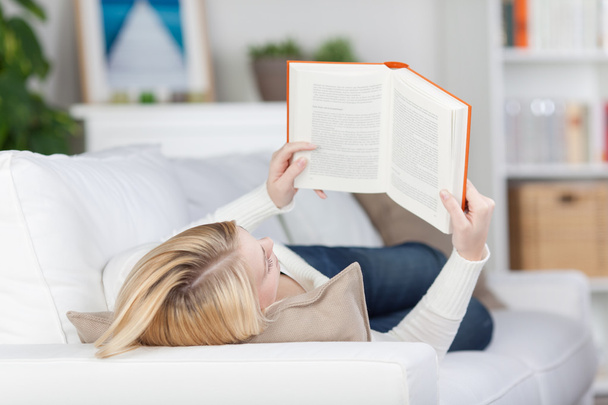 Estudante do sexo feminino leitura livro enquanto deitado no sofá
 - Foto, Imagem