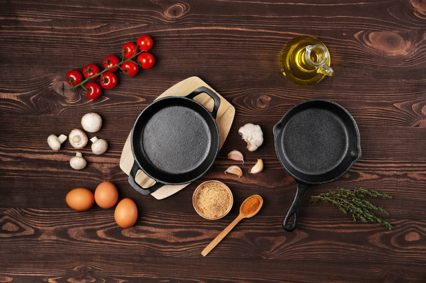 Cast iron skillets and spices on brown wooden culinary background, view from above - Φωτογραφία, εικόνα