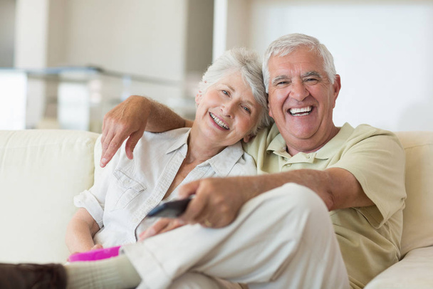 Happy senior couple watching tv on the couch at home in the living room - Foto, Imagen