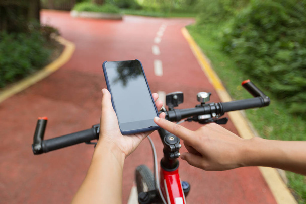 person using smartphone app for navigation while having bike ride on the forest trail - Zdjęcie, obraz