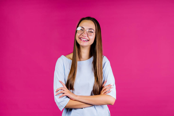 Fashionable girl office worker dressed in a shirt on a pink background. Crossed arms, laughs, round glasses - Fotó, kép