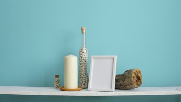 ピクチャーフレームモックアップ付きのモダンな客室の装飾。キャンドルとボトルに岩とパステルターコイズの壁に対する白い棚。鉢植えヘビの植物を置く手 - 映像、動画