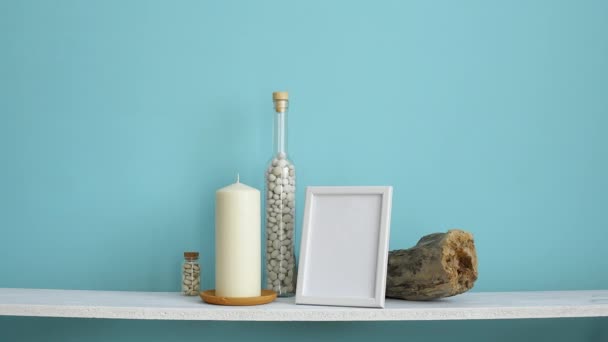 Nowoczesna dekoracja pokoju z wizualizację ramki na zdjęcia. Biała półka przeciw pastelowej turkusowej ścianie ze świecą i kamieniami w butelce. Ręczne odkładanie doniczkowa soczyste rośliny - Materiał filmowy, wideo