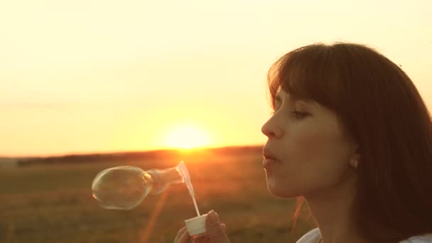 Beautiful woman blowing transparent soap bubbles and smiling. Slow motion. young girl playing in park and blowing bubbles. Beautiful girl blowing soap bubbles in park in spring, summer and smiling. - Footage, Video