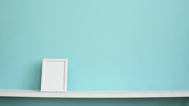 Moderna decoración de la habitación con marco de imagen maqueta. Estante blanco contra la pared de color turquesa pastel y la mano poner en maceta planta schefflera
. - Imágenes, Vídeo