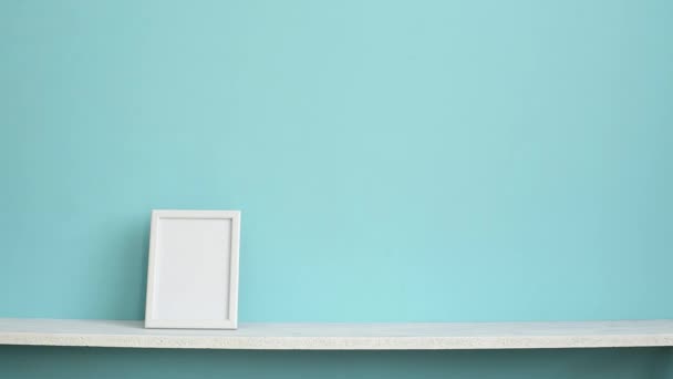Moderna decoración de la habitación con marco de imagen maqueta. Estante blanco contra la pared de color turquesa pastel con la mano poniendo planta de serpiente maceta
. - Imágenes, Vídeo