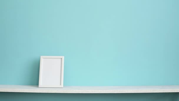 Moderna decoración de la habitación con marco de imagen maqueta. Estante blanco contra la pared de color turquesa pastel con la mano poniendo planta suculenta maceta
. - Imágenes, Vídeo