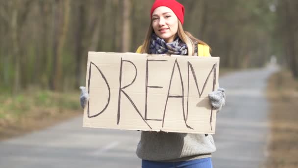 Dziewczyna autostopem pobyt na pustej drodze w drewnie z plakatem marzenie.  - Materiał filmowy, wideo
