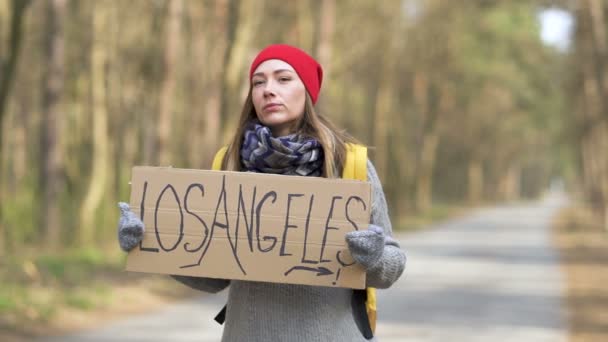 Hitchhiking girl permanecer en la carretera en madera con cartel de Los Ángeles. Equipo de viaje
 - Imágenes, Vídeo