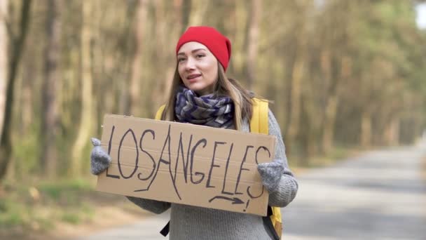 Chica autoestopista permanecer en la carretera vacía en madera con cartel de Los Ángeles. El viaje es vida
 - Imágenes, Vídeo