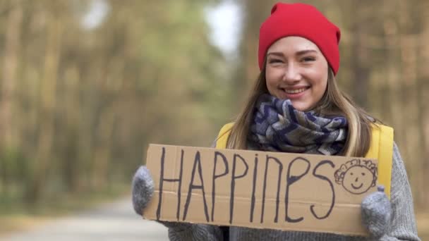 Χαρούμενο κορίτσι με οτοστόπ μείνετε σε άδειο δρόμο σε ξύλο με αφίσα Καλιφόρνια. Η ζωή στο ταξίδι  - Πλάνα, βίντεο