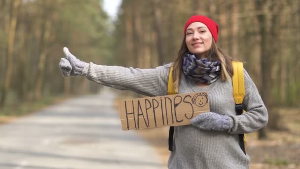 Feliz chica emocional autoestop estancia en camino vacío en madera con cartel de California
.  - Imágenes, Vídeo