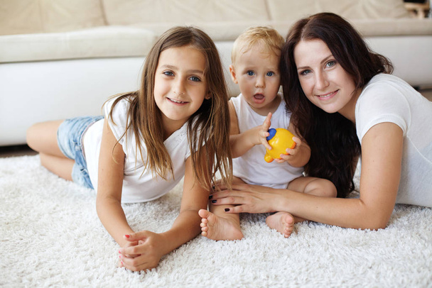Portrait of a mother with her baby and pre-teen children having fun on white carpet in living room at house - Фото, зображення