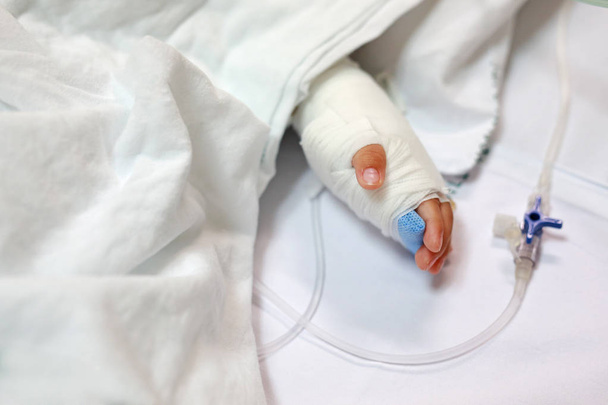 Close up baby hand on patient's bed in hospital with saline intravenous. Baby admitted at hospital. Kid patients have IV tube. - Valokuva, kuva