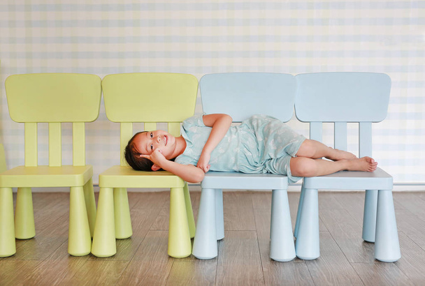 Happy child preschool girl in a Kindergarten room lying on plastic baby chair. - 写真・画像