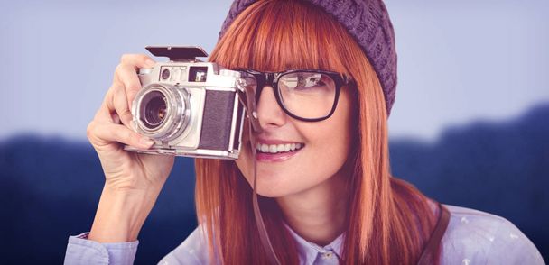 Smiling hipster woman taking pictures with a retro camera against blurred mountains - Foto, imagen