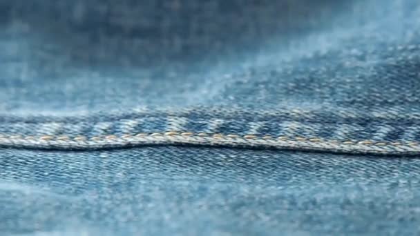 Blue jeans laying on the table. Macro dolly shot. Selective soft focus. Camera moving along side seam of jeans. Texture of denim, background from denim texture close up. - Video, Çekim