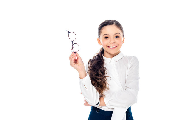 adorable smiling schoolgirl in formal wear holding glasses and posing Isolated On White with copy space - 写真・画像